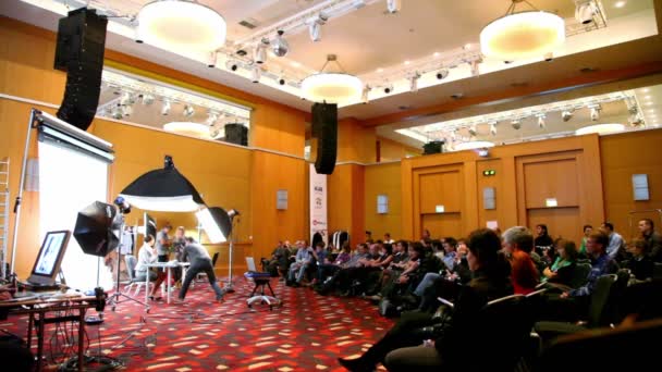 Model sits at table with laptop at demonstration of studio shooting at conference Stockinrussia 2010 — Stock Video