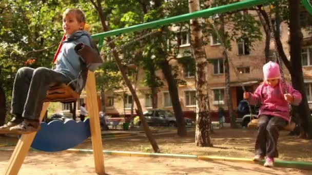 Ragazzo e bambina ondeggiano sull'altalena al parco giochi — Video Stock