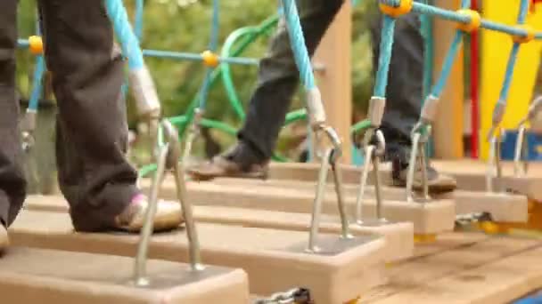Niña y niño se balancean en colgar escaleras en el patio de recreo — Vídeos de Stock