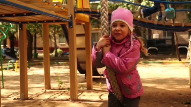 Klein meisje hangt op touw op speeltuin en zwaaien — Stockvideo