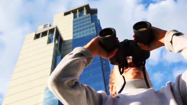 Inquisitive boy looks through binoculars on background of skyscrapers, then turns — Stock Video