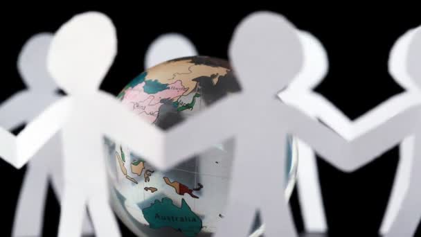 Паперові люди стоять, тримаючись за руки і обертаються навколо прозорого глобуса — стокове відео