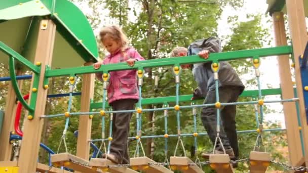 Menina e menino balançam em pendurar os degraus no playground — Vídeo de Stock