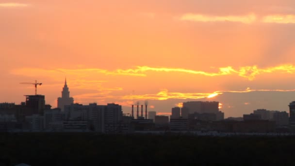 Ciudad de pie contra el cielo en la puesta del sol donde el sol se esconde en las nubes — Vídeos de Stock