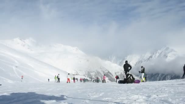 Skiërs naar beneden gaan van berg tegen wolken en blauwe hemel — Stockvideo