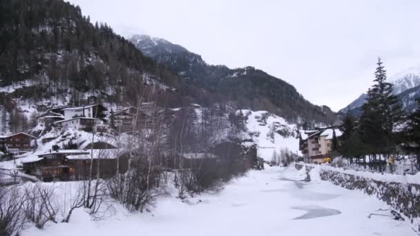 In der Nähe von Hotels und Häusern im Tal gibt es einen Fluss, der mit Eis bedeckt ist — Stockvideo