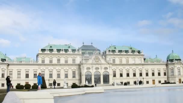 Toeristen bezoeken kasteel belvedere die tegen blauwe hemel vóór vijver staat — Stockvideo