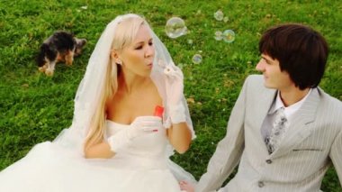 Newly-married couple sits near to doggie and bride starts up soap bubbles