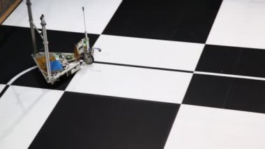robot oyuncak araba üzerinde büyük satranç tahtası çizilmiş bir hat boyunca taşır.