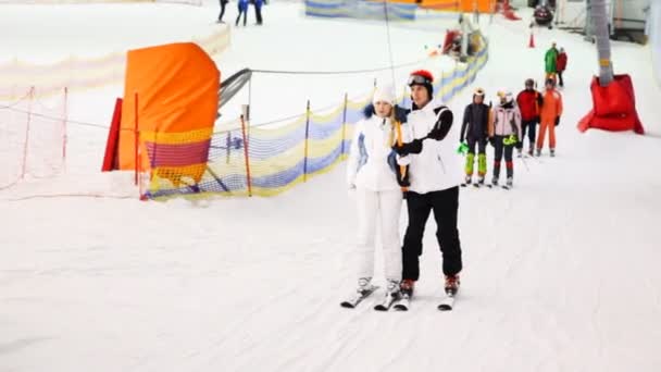 Instruktor s holkou držet nějakou hůl a jít nahoru na kopec na lyžích — Stock video