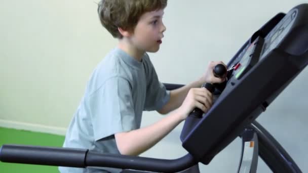 Liten pojke går på löpband och ser till panel med händerna på handtag — Stockvideo