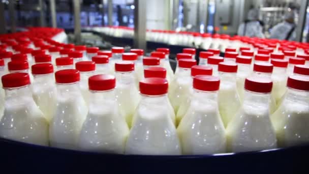 Un montón de botellas de plástico con leche y tapas rojas en la fábrica se mueve en círculo — Vídeos de Stock