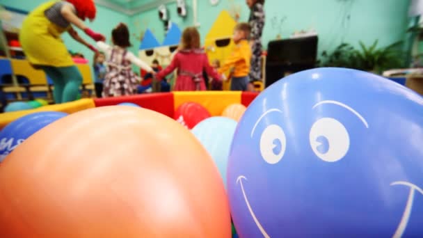 インフレータブル ボールは笑みを浮かべて、それの後ろにデフォーカスのピエロと介護者と遊んでいる子供たち — ストック動画