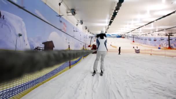 Girl in white dress goes down to ski on slope holding rope — Stock Video