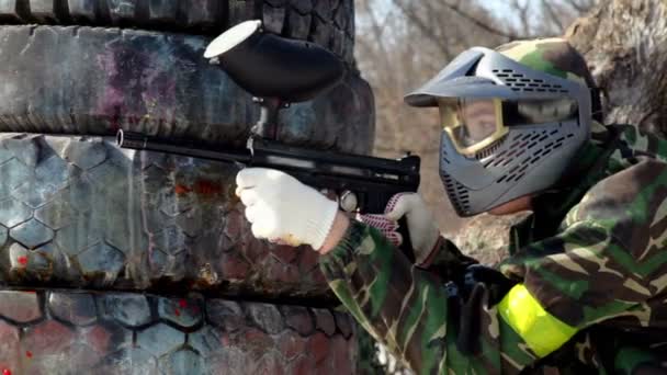 Pojke sitta i bakhåll bakom däck med paintball gevär och skjuter — Stockvideo