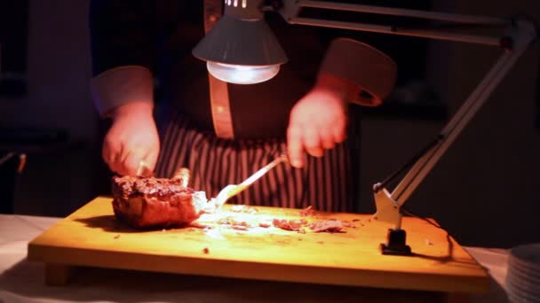 Las manos del cuchillo de cocina gran pedazo de carne humeante a la luz de la lámpara — Vídeos de Stock