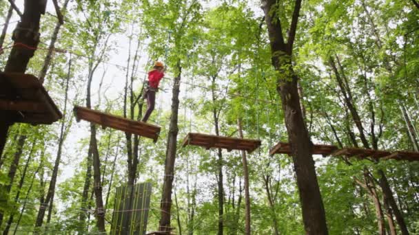Dziewczyna idzie na zawieszone przez kable na drzewa, drewno, deski — Wideo stockowe