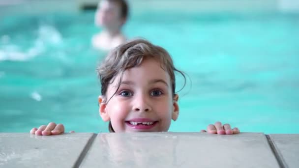 Malá holčička skáče ve vodě u okraje bazénu, její bratr na pozadí — Stock video
