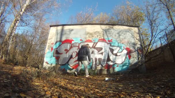 Adolescent dessiner des graffitis sur le mur en automne sur l'île de Losinyj — Video