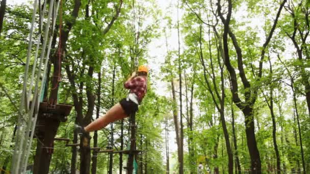 Дівчина рухається вниз підвішеною на кабелі в дереві між деревами — стокове відео