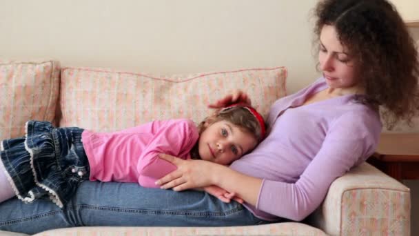 Dziewczynka leży na jej matka nogi na kanapie — Wideo stockowe