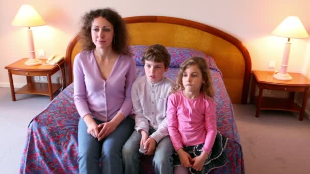 Мама и ее дети мальчик и девочка сидят на диване и смотрят телевизор — стоковое видео