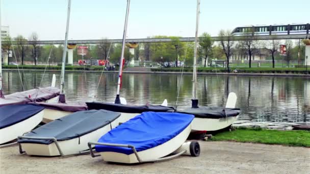Кілька човнів лежали поблизу ставка, поїзда і міського руху — стокове відео