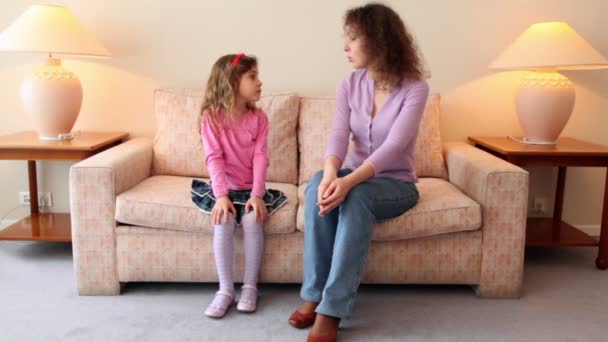 Madre se sienta en el sofá con su hijita y le cuenta algo — Vídeos de Stock
