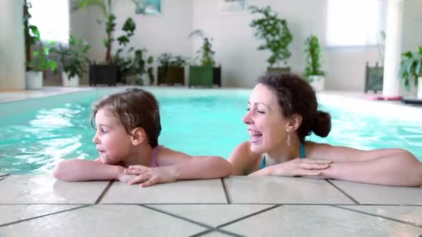 Niña con su madre se quedan en el borde de la piscina cubierta — Vídeo de stock