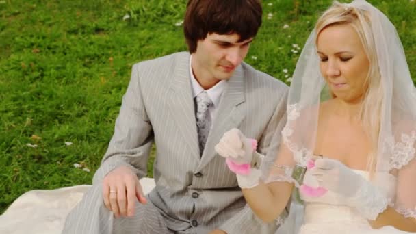 Couple nouvellement marié assis sur la prairie sont attachés aux menottes — Video