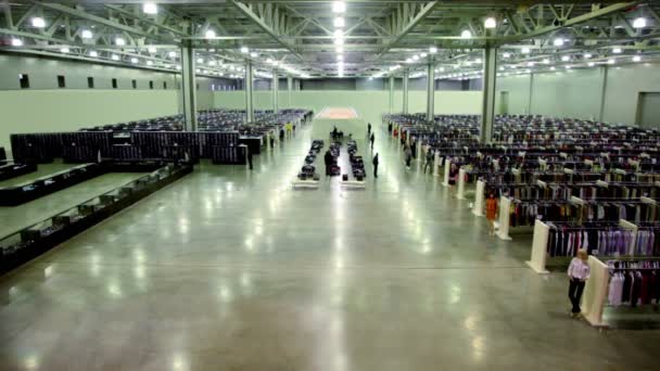 As pessoas caminham e assistem mercadorias dentro da loja de roupas em um enorme hangar — Vídeo de Stock