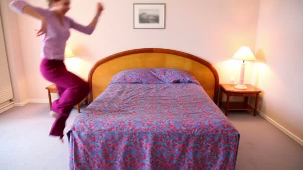 Young woman runs and jumps on bed then lies on it — Stock Video