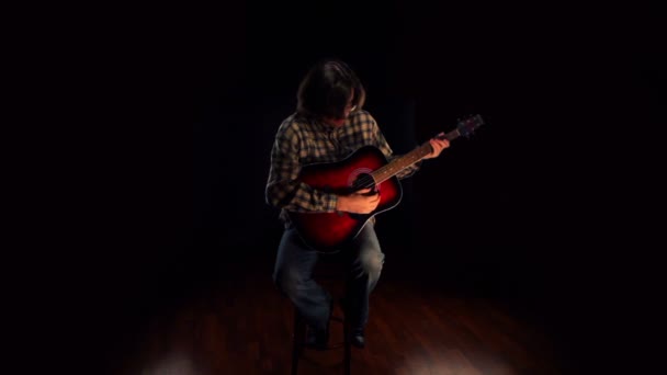 Man wearing glasses sits on chair and plays guitar at dark — Stock Video