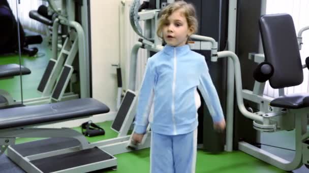 Little girl exercises with dumbbells at background of training equipment near mirror — Stock Video