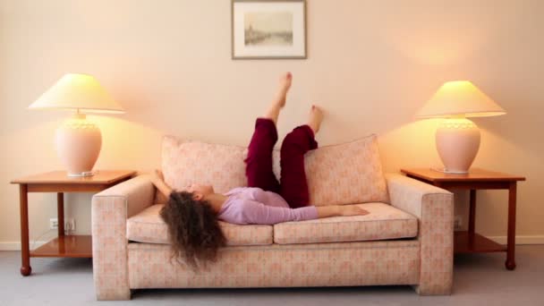 Young woman lies on sofa and shake legs at room with lamps on each side — Stock Video