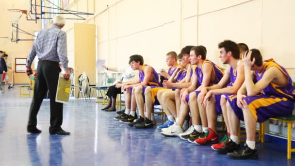 Jogadores de basquete sentam-se no banco, e o treinador diz que no intervalo do jogo estudantil — Vídeo de Stock