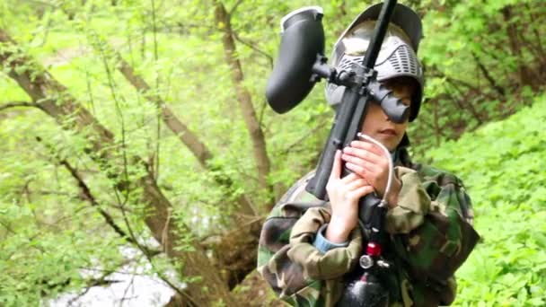 Garçon se tient avec pistolet de paintball à l'arrière-plan de feuilles vertes — Video