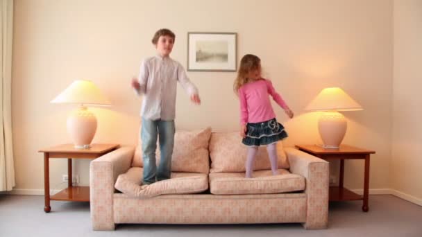 Two kids jump on sofa at room with lamps on each side — Stock Video