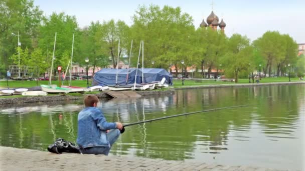 Visser op vijver in stadspark bij achtergrond van kerk achter bomen — Stockvideo