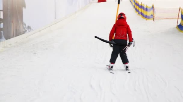 Pequeno esquiador sentado no punho desce colina no centro desportivo — Vídeo de Stock