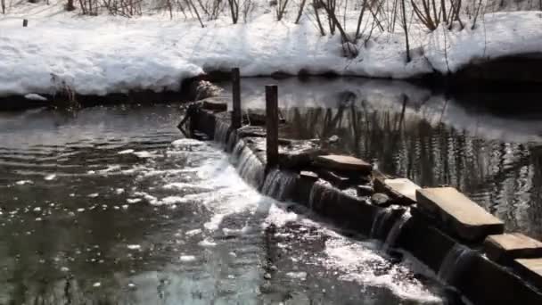 Snow lay on coast of river with small waterfall on dam — Stock Video