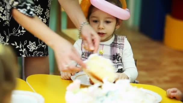 Дитячий мсьє розкладає шматочки торта дітям, які сидять за столом в дитячому садку — стокове відео