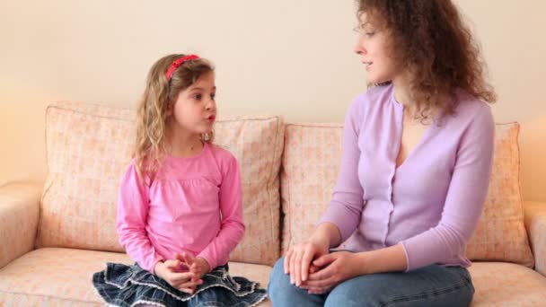 La niña se sienta en el sofá con su madre y le cuenta algo — Vídeos de Stock