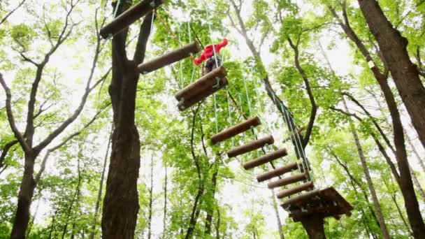 Girl fixed on insurance, jumps on suspended by ropes on trees to logs — Stock Video