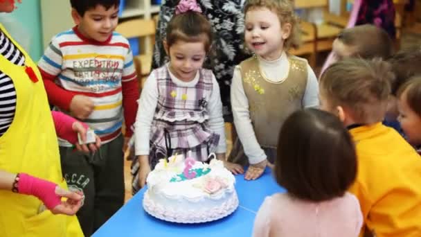 Payaso enciende vela en forma de tres en la torta, chica soplando y niños abofeteando — Vídeo de stock