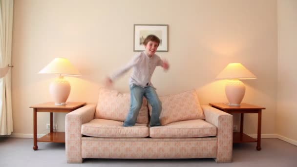 Little boy jumps on sofa at room with lamps on each side — Stock Video