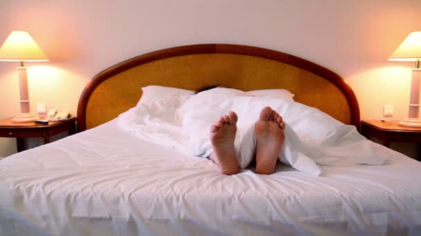 Kadın battaniyenin altında yatakta yatıyordu ve bootless ayak taşır — Stok video
