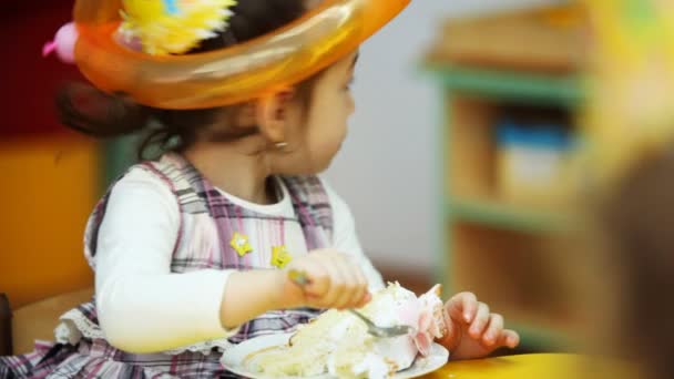 Menina senta-se e come doce rosa com bolo de aniversário — Vídeo de Stock