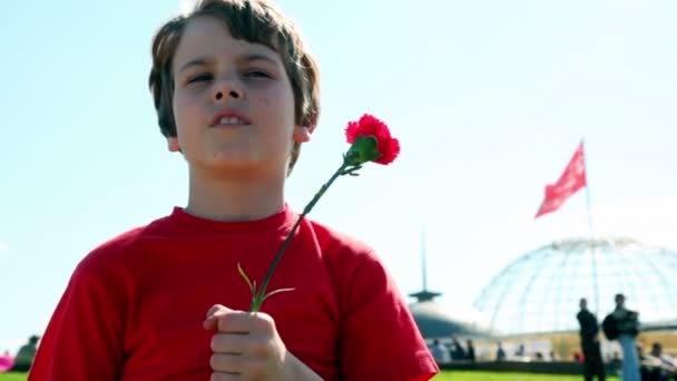 Niño pequeño con pie de flores rojas en el fondo de la bandera roja — Vídeos de Stock