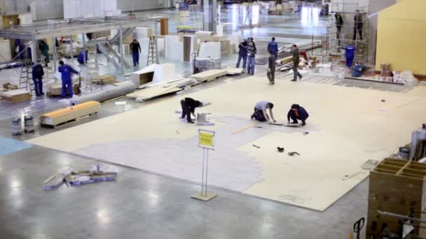 Flera arbetare göra golvet och andra bygga hus i utställningen hangar — Stockvideo